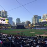 A packed baseball stadium with players on the infield and a large video board displaying colorful graphics; 'petco park' sign visible at left.