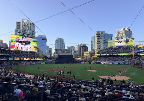 A packed baseball stadium with players on the infield and a large video board displaying colorful graphics; 'petco park' sign visible at left.